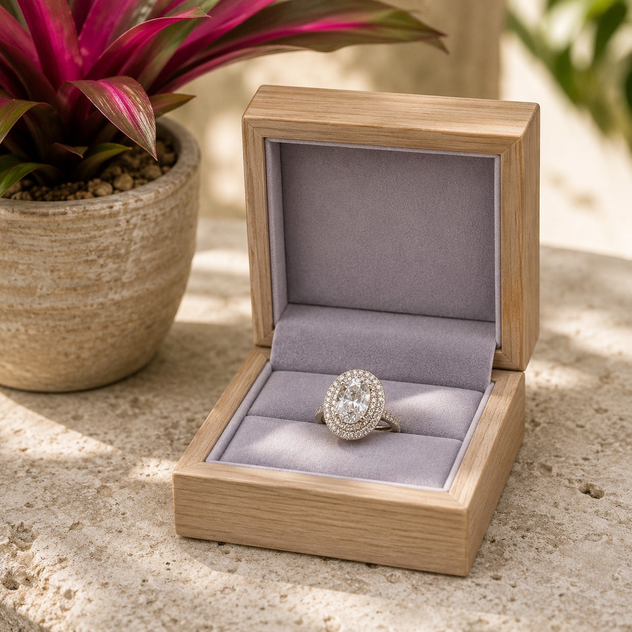 Crystal clear oval halo stainless steel ring showcased in a luxury wooden ring box on a textured stone surface.