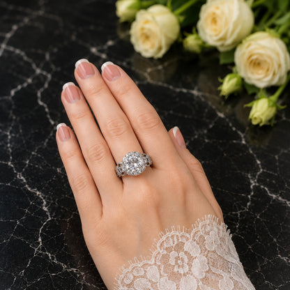 Silver statement ring with sparkling halo center stone worn on a hand with French manicure.