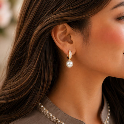 Close-up of a model wearing white pearl drop hoop earrings with baguette crystal detailing.