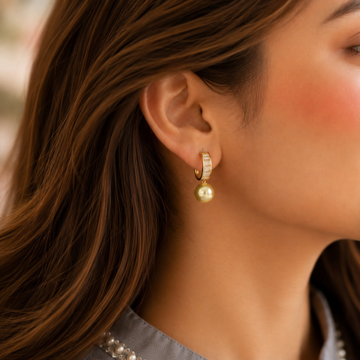 Close-up of a model wearing Golden Olive pearl drop hoop earrings with baguette crystal detailing.