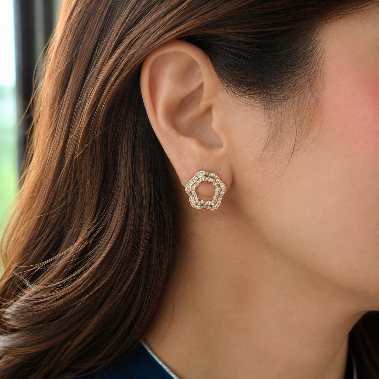 Close-up of gold open-centre floral zircon stud earring worn on ear
