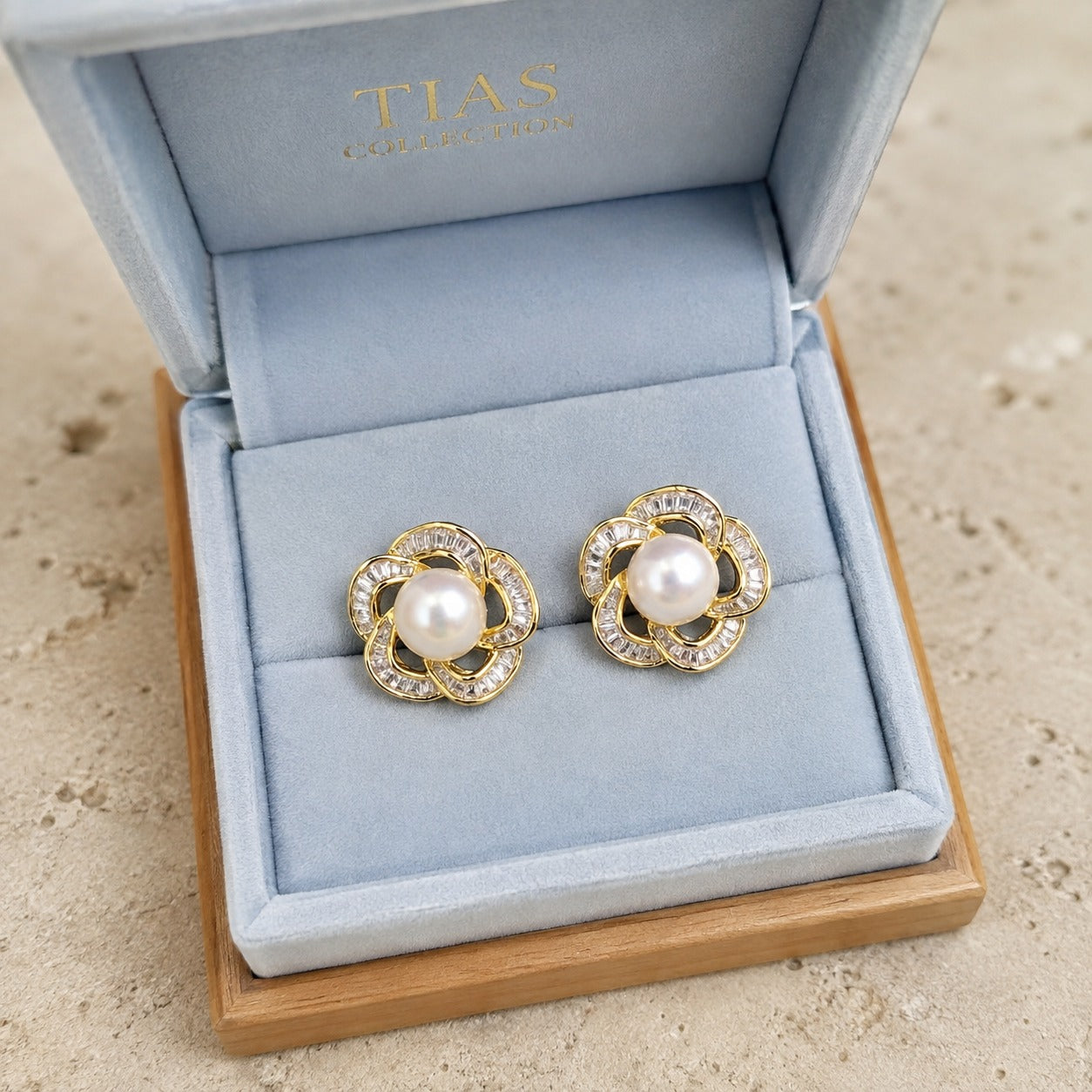 Pearl Loop Stud Earrings in gold with pearl centre and clear stones displayed in blue jewellery bo