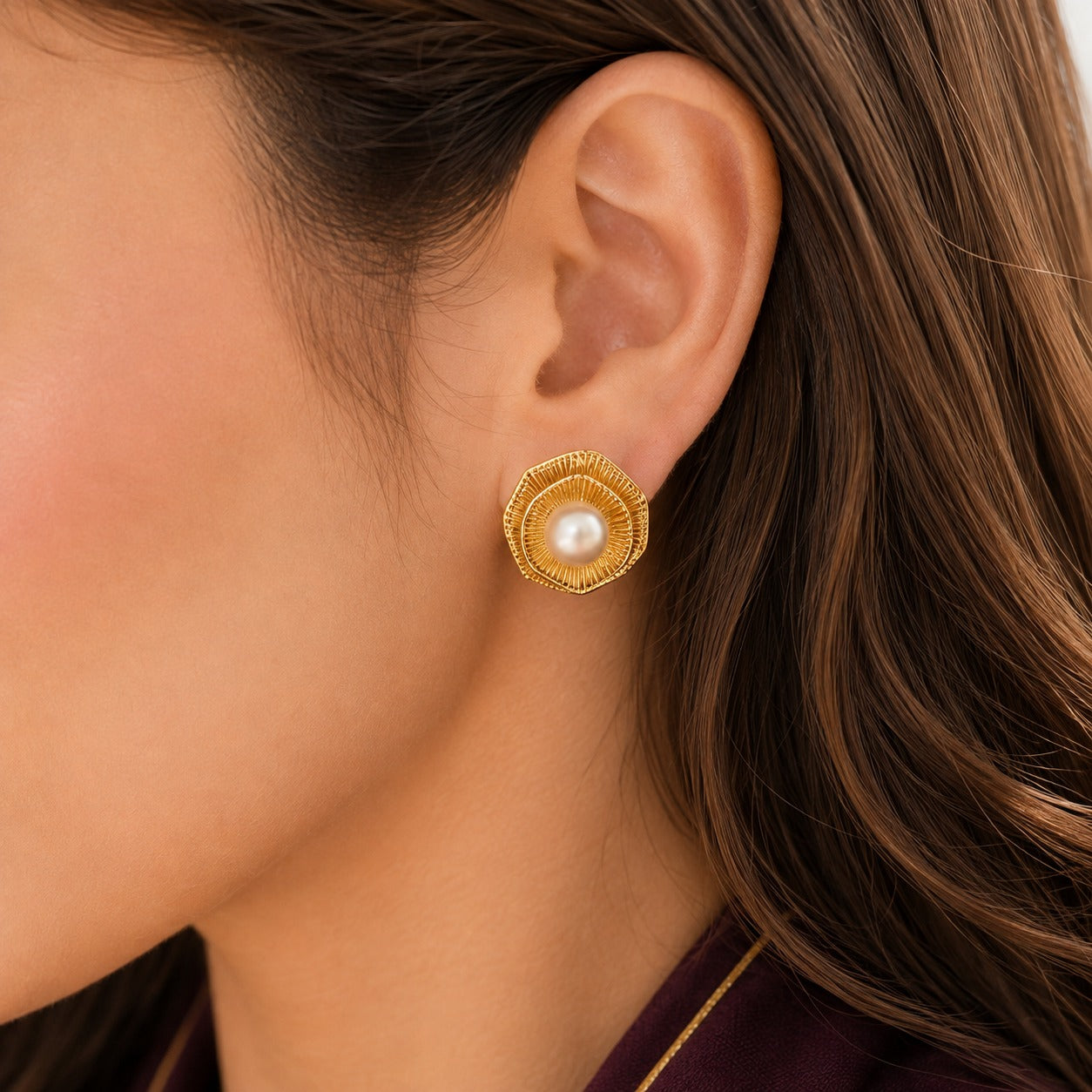  Close up of model wearing gold pearl statement studs with textured circular detailing