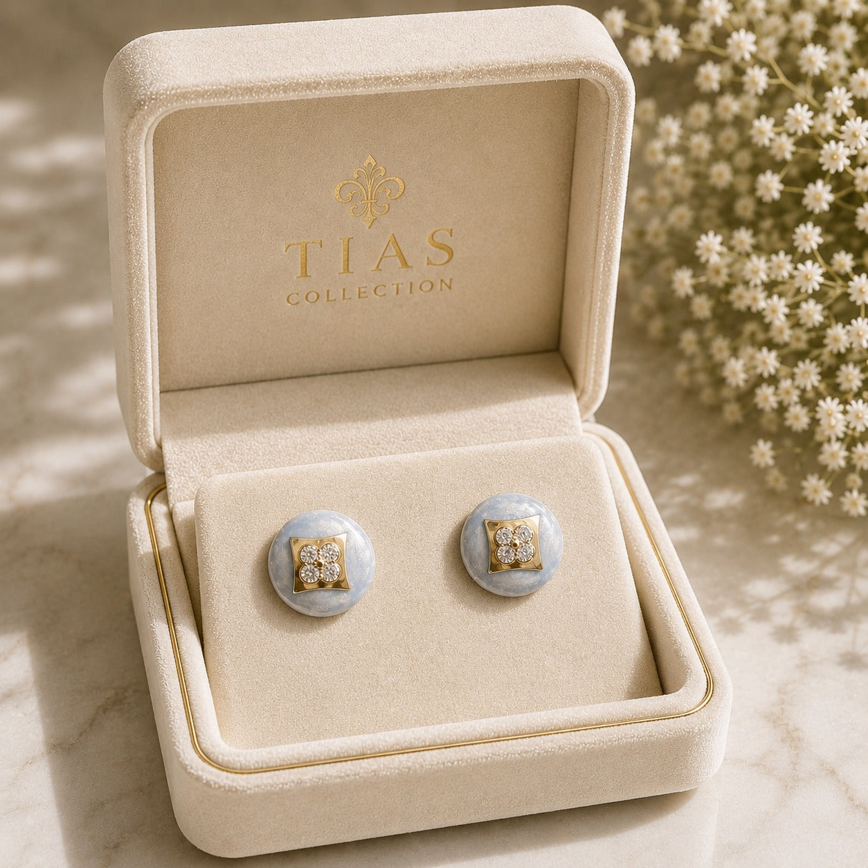 Powder Crest Stud Earrings displayed in a jewellery box with pale blue round bases, geometric gold-tone centres and clear zircon accents.