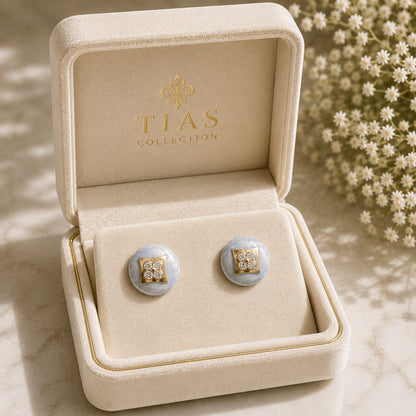 Powder Crest Stud Earrings displayed in a jewellery box with pale blue round bases, geometric gold-tone centres and clear zircon accents.