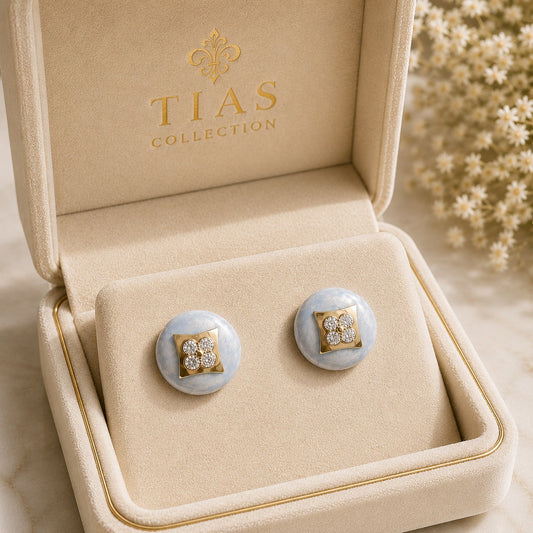 Powder Crest Stud Earrings displayed in a jewellery box with pale blue round bases, geometric gold-tone centres and clear zircon accents.