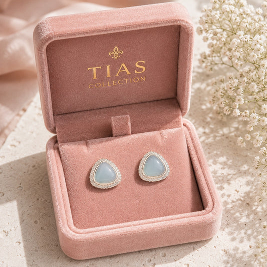 Pair of Glacier Cove Stud Earrings displayed in a blush pink jewellery box, featuring smooth ice-blue centres with clear zircon detailing.