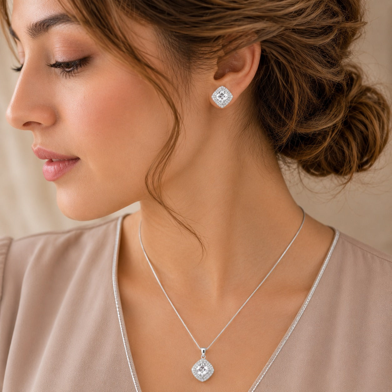 Model wearing matching clear zircon cushion stud earrings and pendant necklace in a silver-tone setting.