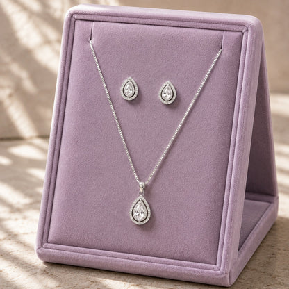 Clear zircon teardrop pendant necklace and matching stud earrings displayed on a soft lilac jewellery stand.