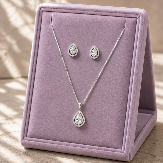 Clear zircon teardrop pendant necklace and matching stud earrings displayed on a soft lilac jewellery stand.