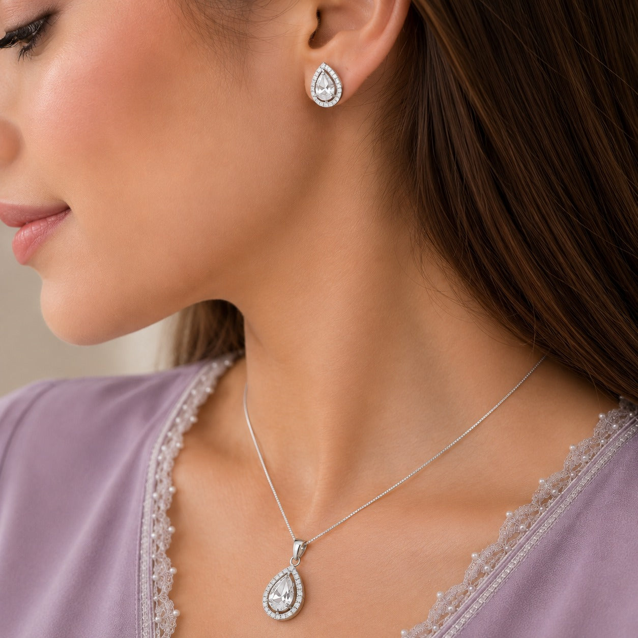 Close-up of clear zircon teardrop pendant and matching stud earrings in a silver-tone setting worn by a model.