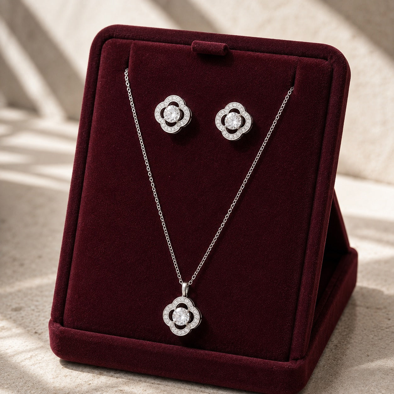 Vela Loop clear zircon pendant necklace and matching stud earrings displayed on a burgundy velvet jewellery stand.