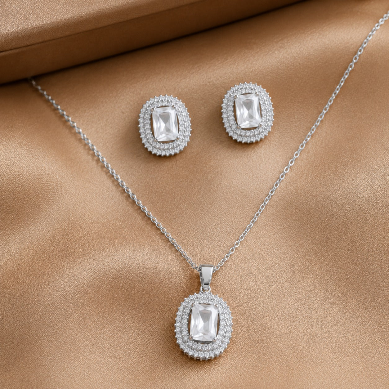 Lucent Frame matching clear zircon pendant and stud earrings displayed in a champagne-tone satin cloth