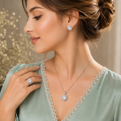 Model wearing matching clear zircon stud earrings, pendant necklace and statement ring in a silver-tone setting.