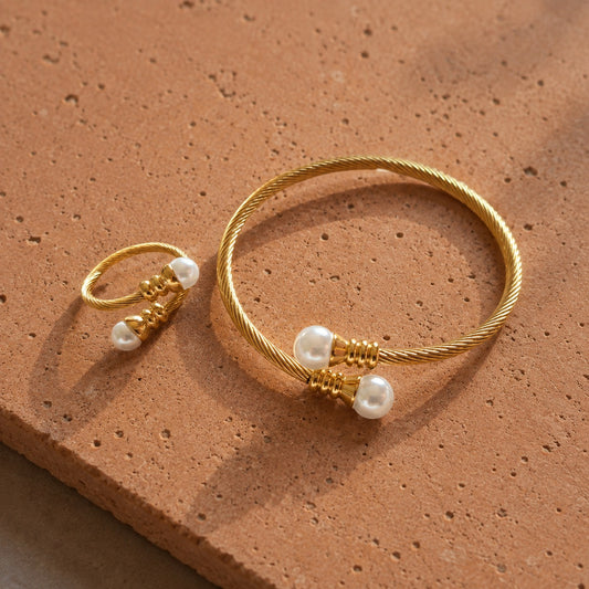 Close-up of gold-tone pearl-ended bracelet and matching ring with twisted cable texture displayed on a terracotta surface.