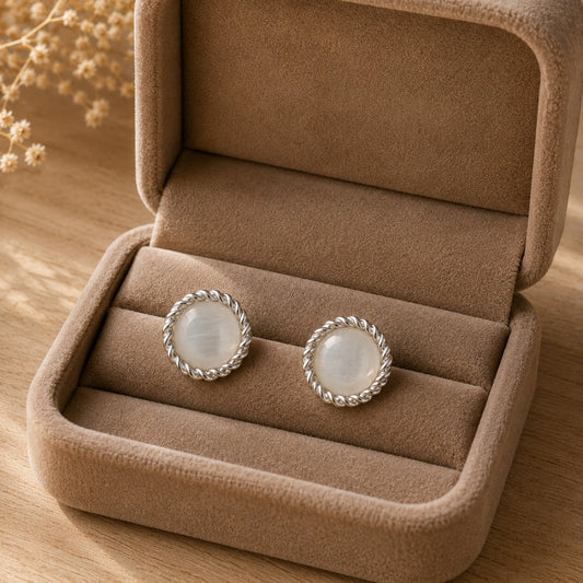 Close-up of pearlescent white round hook back earrings with polished silver-tone rope edging displayed in a soft taupe jewellery box.
