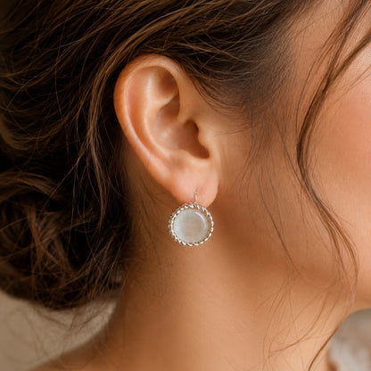 Silver-tone round  hook back earrings with pearlescent white centres and twisted-rope borders worn on the ear.