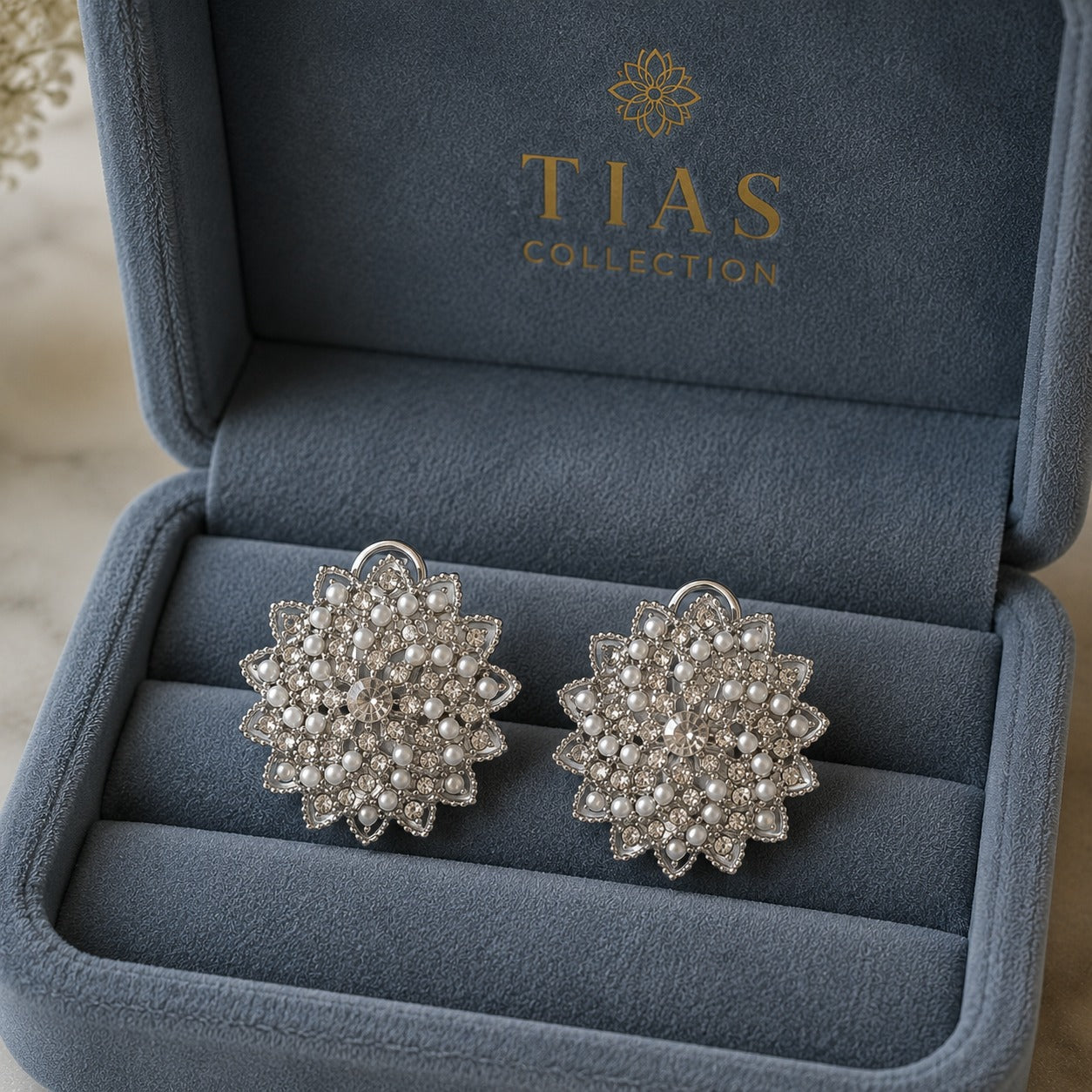 Silver-tone statement clip earrings featuring an intricate radial design embellished with miniature pearls and clear sparkling stones in a box