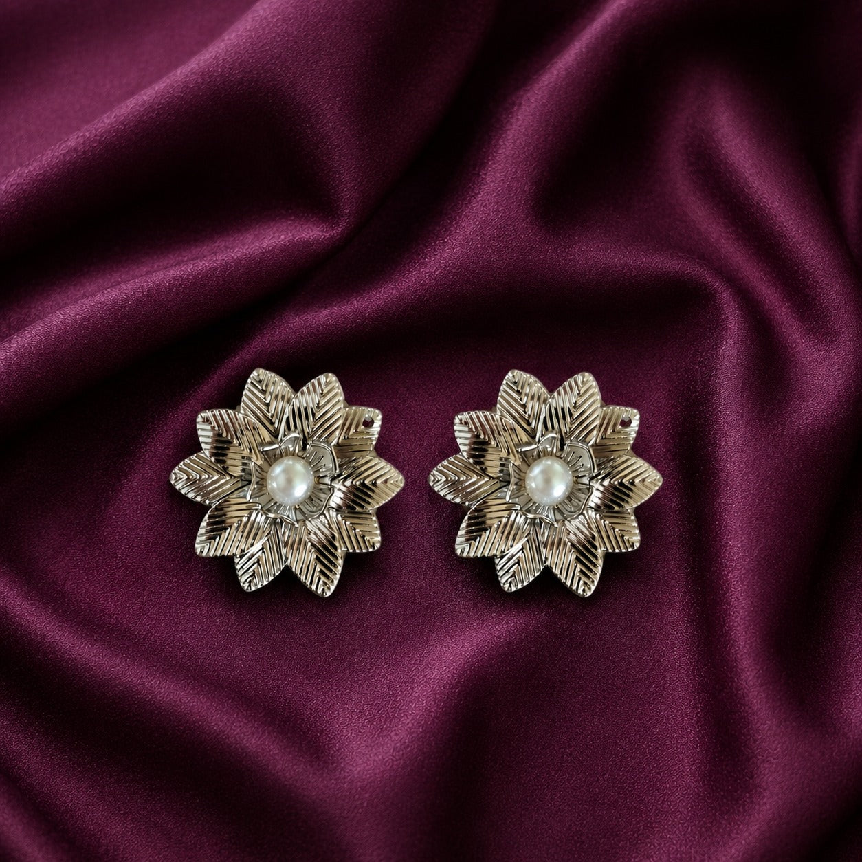 Silver-tone Silver Fern statement earrings with layered textured leaves and pearl centres displayed on plum satin.