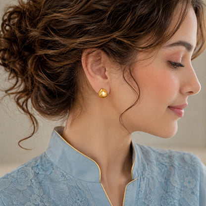 A close-up side profile of a woman wearing a small gold teardrop stud earring 