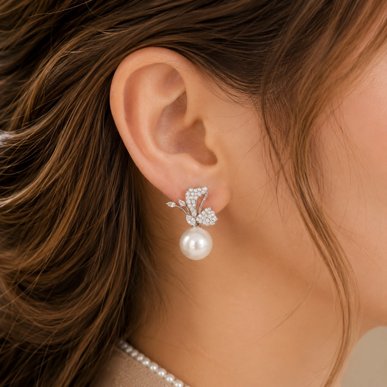 Close up of model wearing silver-tone Pearlwing Earrings featuring clear zircon wing-inspired detailing, marquise accents and luminous round pearl drops.