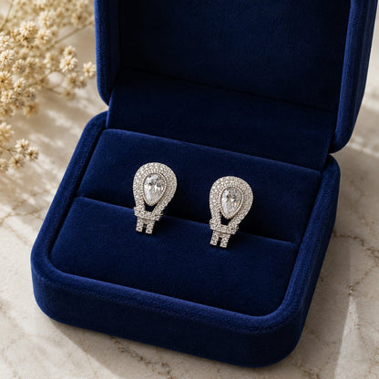 Silver-tone teardrop earrings with clear pear-cut zircon centres and pavé detailing displayed in a navy velvet jewellery box.