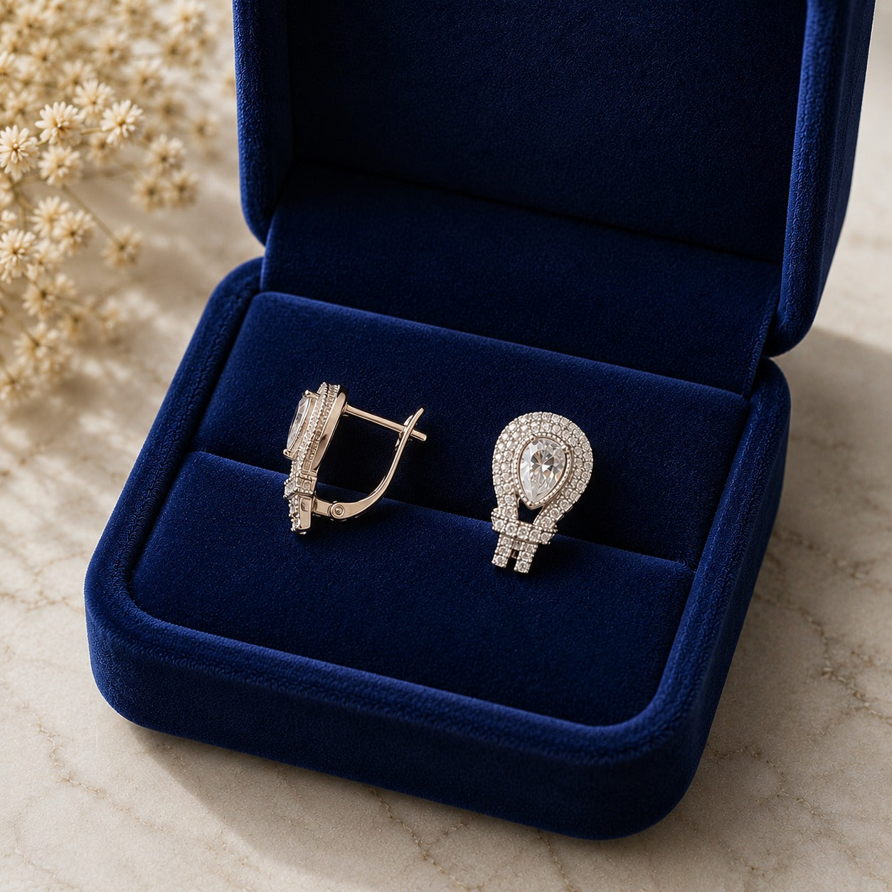 Pair of silver-tone teardrop zircon earrings with pear-cut clear centre stones displayed in a navy blue velvet jewellery box.