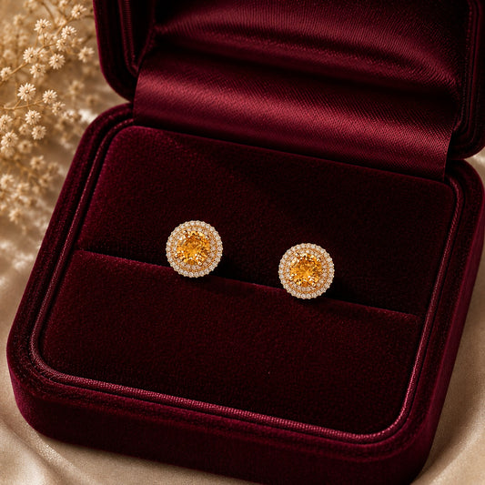Pair of gold-tone stud earrings with golden-yellow centre stones and clear zircon borders displayed in burgundy velvet jewellery bo