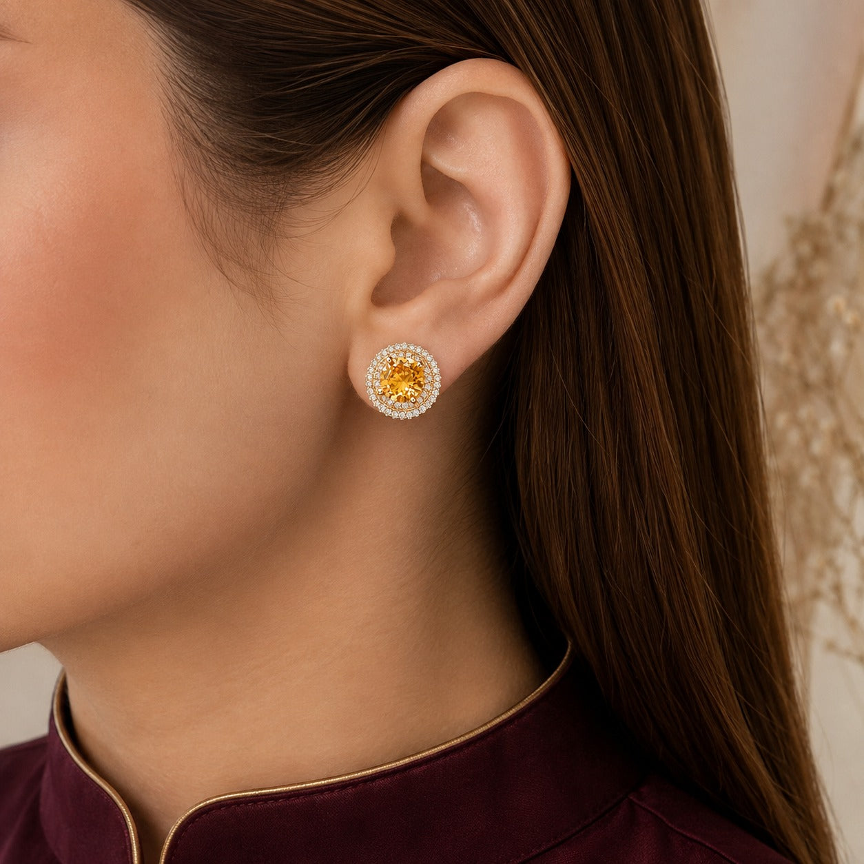 Golden-yellow centre stone stud earring with double clear zircon border in gold-tone setting worn on ear