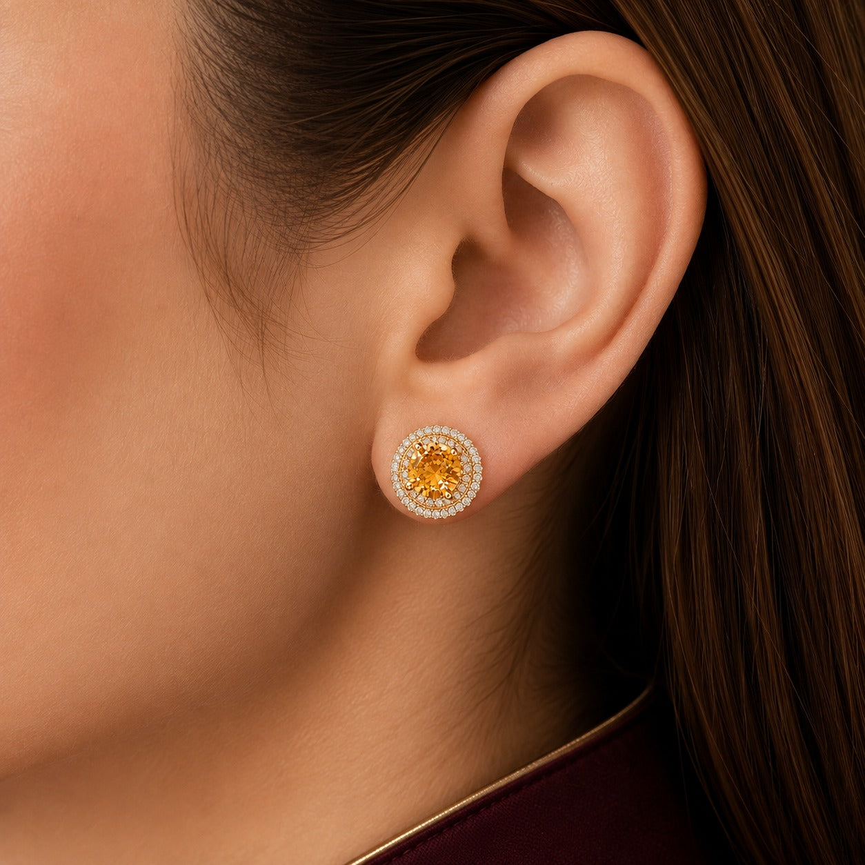 Golden-yellow centre stone stud earring with double clear zircon border in gold-tone setting worn on ear