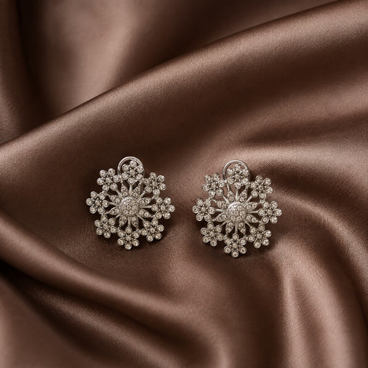 Pair of silver-tone floral statement earrings with intricate clear crystal clusters and openwork detailing displayed on brown satin.