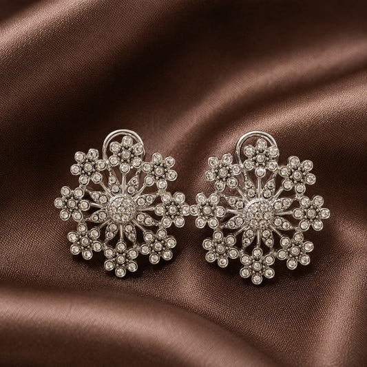 Pair of silver-tone floral statement earrings with intricate clear crystal clusters and openwork detailing displayed on brown satin.