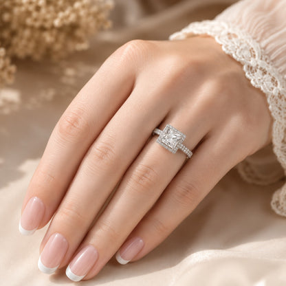  Crystal Clear Square-cut statement ring worn on a manicured hand, showcasing the faceted centre stone, sparkling halo and stone-set band