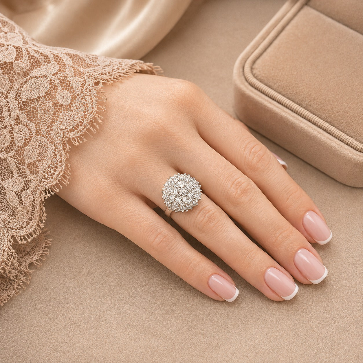 A close-up of a hand wearing a sparkling round cluster ring with clear stones, styled with a beige lace sleeve and a matching jewelry box in the background.