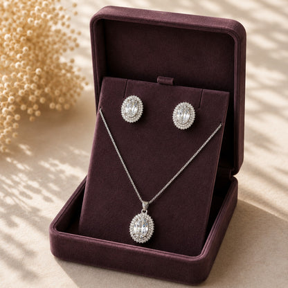 Silver-tone earrings and pendant necklace set with large oval-cut clear zircons and double zircon borders displayed in a deep plum jewellery box.