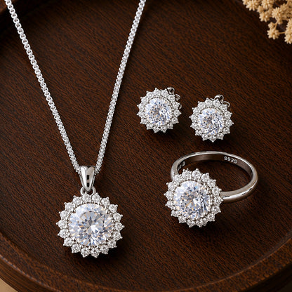 S925 silver earrings, pendant necklace and matching ring set with round clear centre stones and detailed clear stone borders displayed on dark wood.