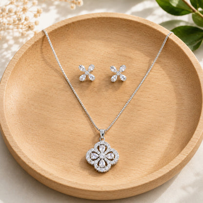 Petal Loop S925 silver pendant and earring set with clear pear-cut zircons arranged in four-petal designs on a light wooden surface.
