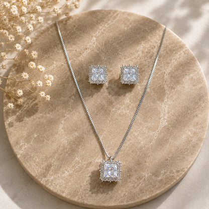 Lucent Frame silver square pendant and matching earrings with clear faceted centre stones and zircon borders displayed on beige marble.