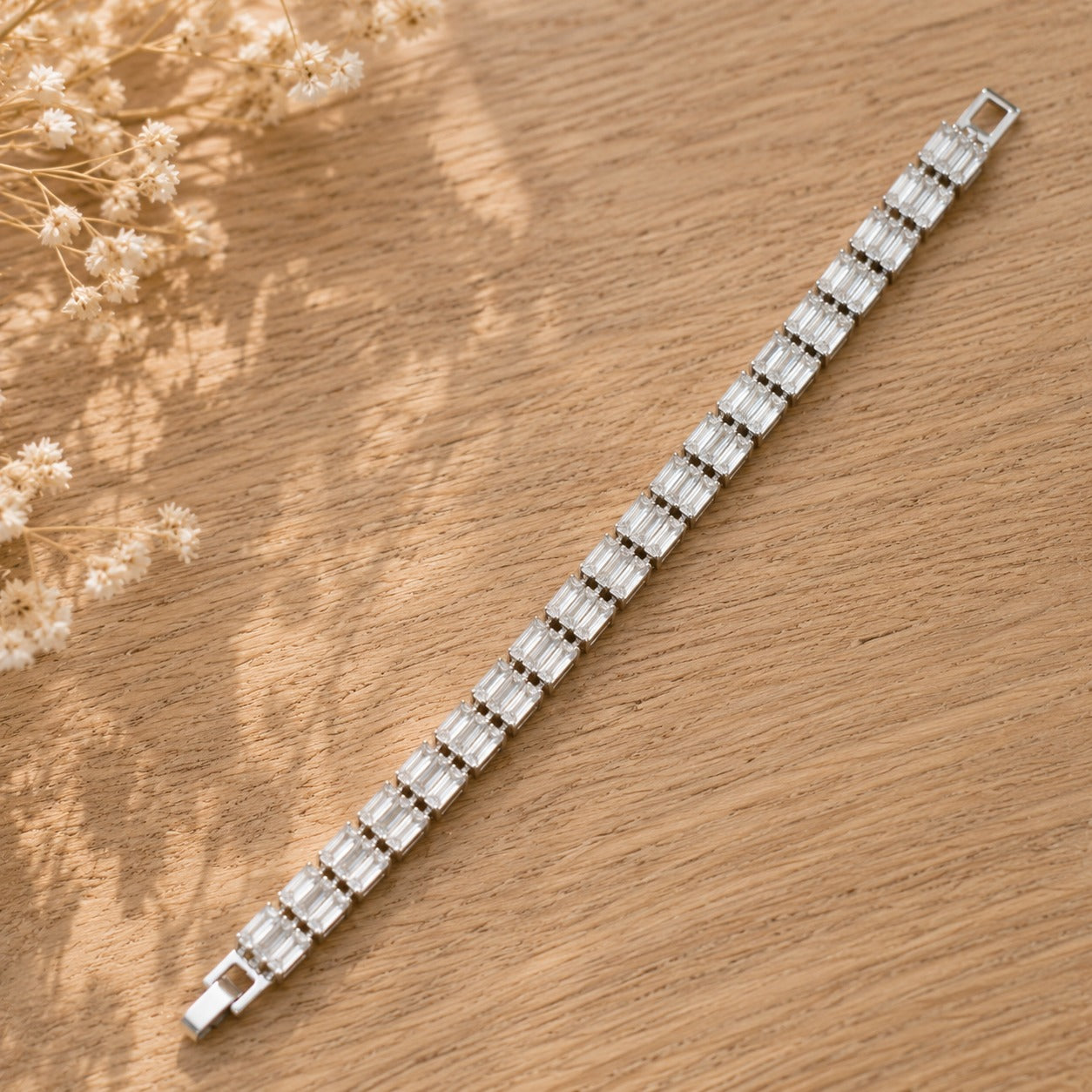 Full-length silver-tone bracelet with continuous clear baguette-cut stones and secure clasp displayed on natural wood.
