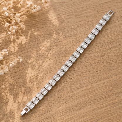 Full-length silver-tone bracelet with continuous clear baguette-cut stones and secure clasp displayed on natural wood.