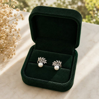 Pair of silver-tone pearl stud earrings with marquise-cut clear stones arranged in delicate leafy branches, displayed in a forest-green jewellery box