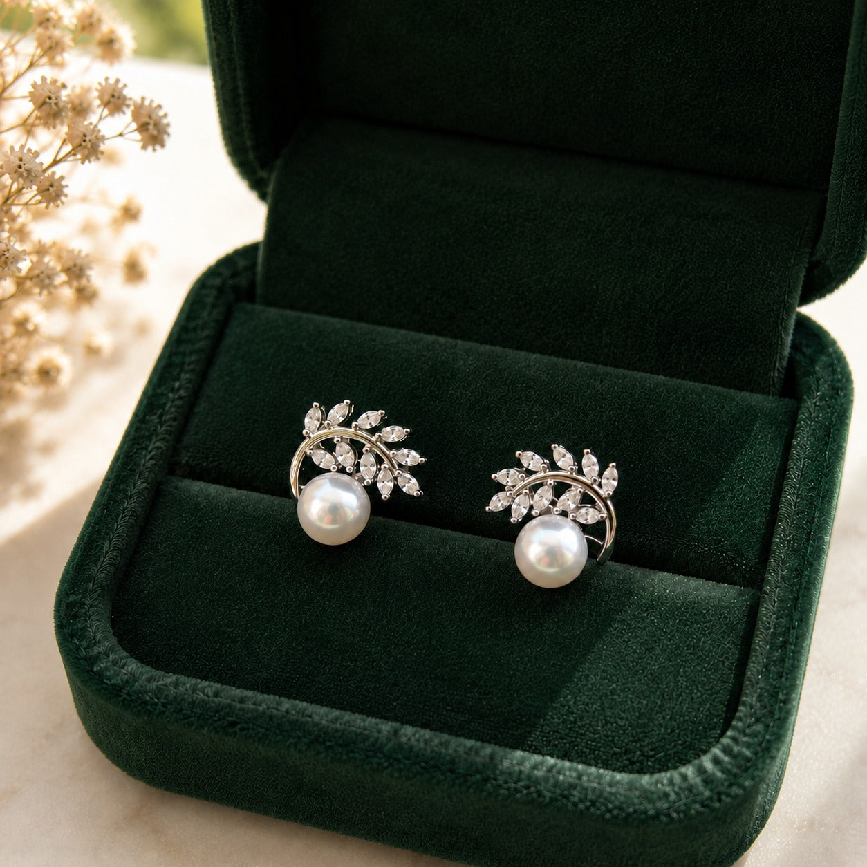 Pair of silver-tone pearl stud earrings with marquise-cut clear stones arranged in delicate leafy branches, displayed in a forest-green jewellery box.