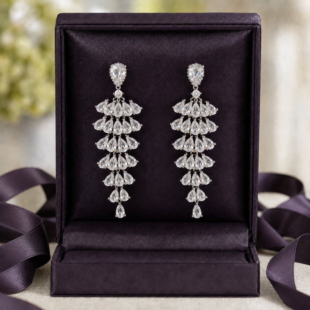 S925 Cascade Prism Drop Earrings with multiple tiers of pear-cut clear zircon stones displayed in a deep plum jewellery box.