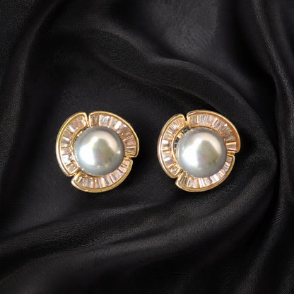Gold-tone Pearl Circuit Stud Earrings with luminous round pearl centres and segmented baguette-cut clear stone frames displayed on black fabric.