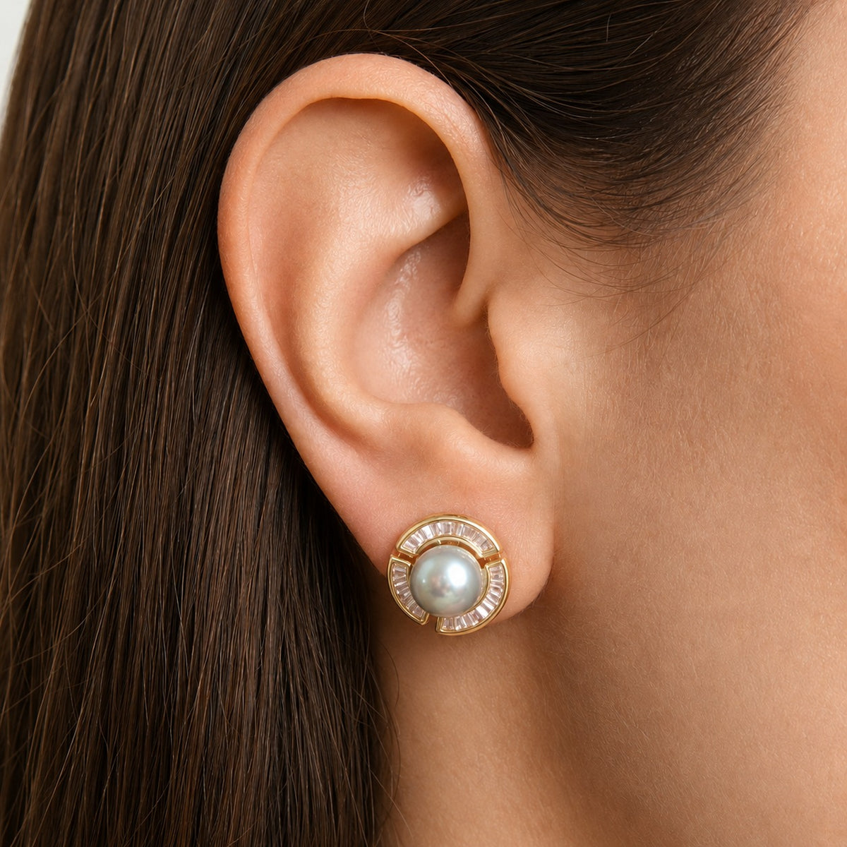 Close-up of a Gold Pearl Circuit Stud Earring worn on the ear, featuring a luminous central pearl surrounded by geometric baguette-cut clear stones.