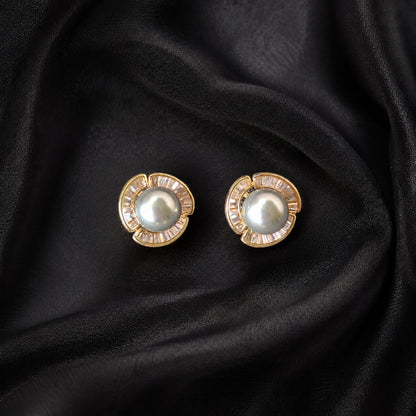Gold-tone Pearl Circuit Stud Earrings with luminous round pearl centres and segmented baguette-cut clear stone frames displayed on black fabric.