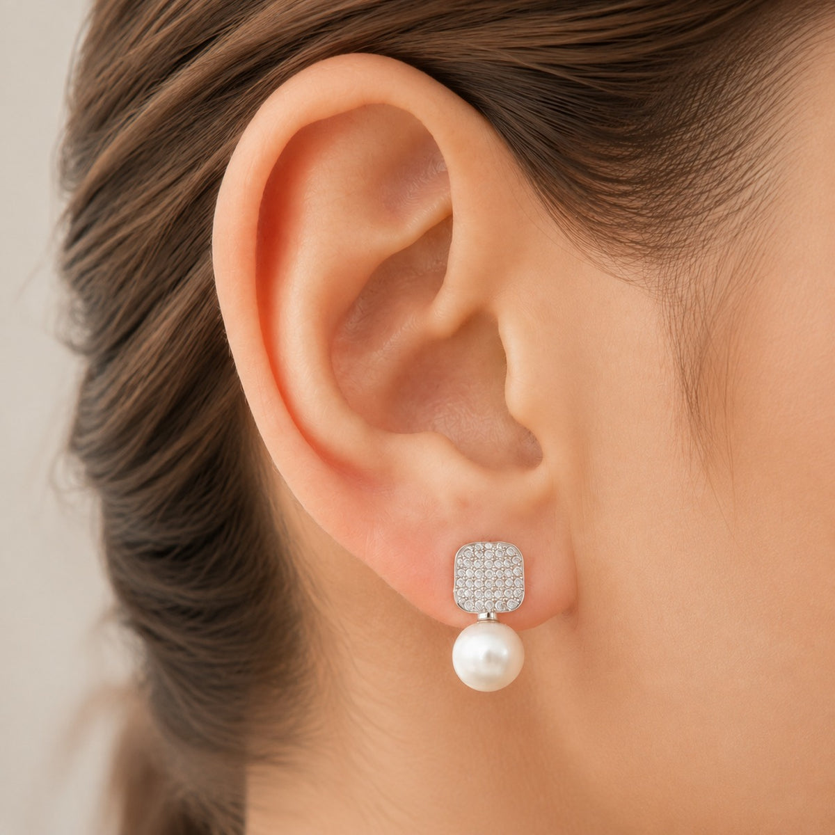 Close-up of Pearl Grid Drop Earring worn on the ear, featuring a crystal-detailed rounded-square top with a smooth white pearl suspended below.