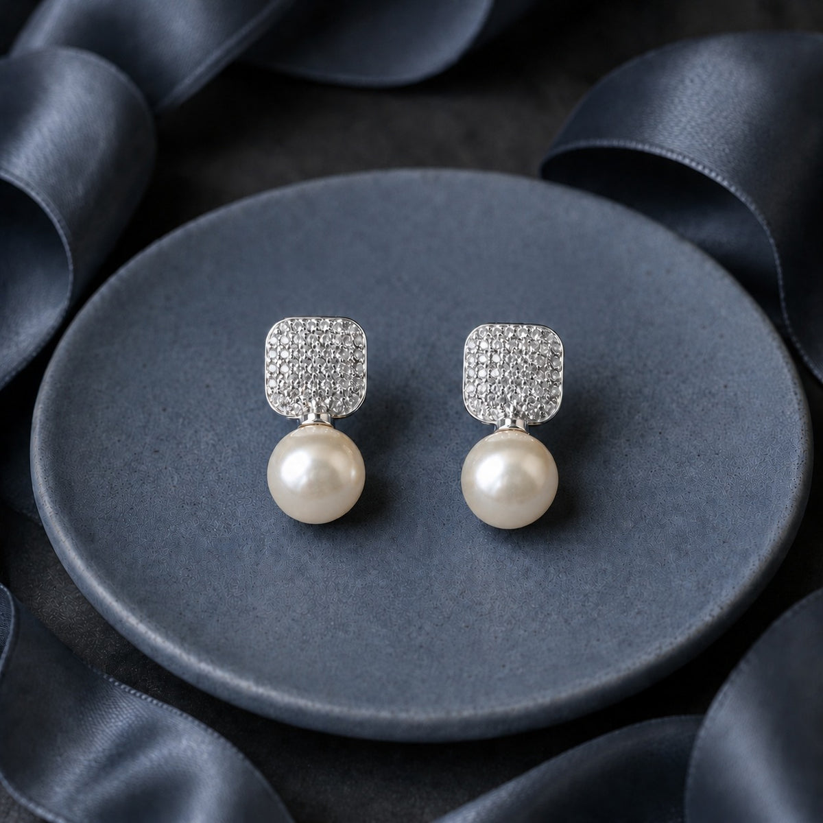 Pearl Grid Drop Earrings featuring rounded-square silver-tone tops with tiny clear stones and luminous white pearl drops, displayed on a dark grey surface.