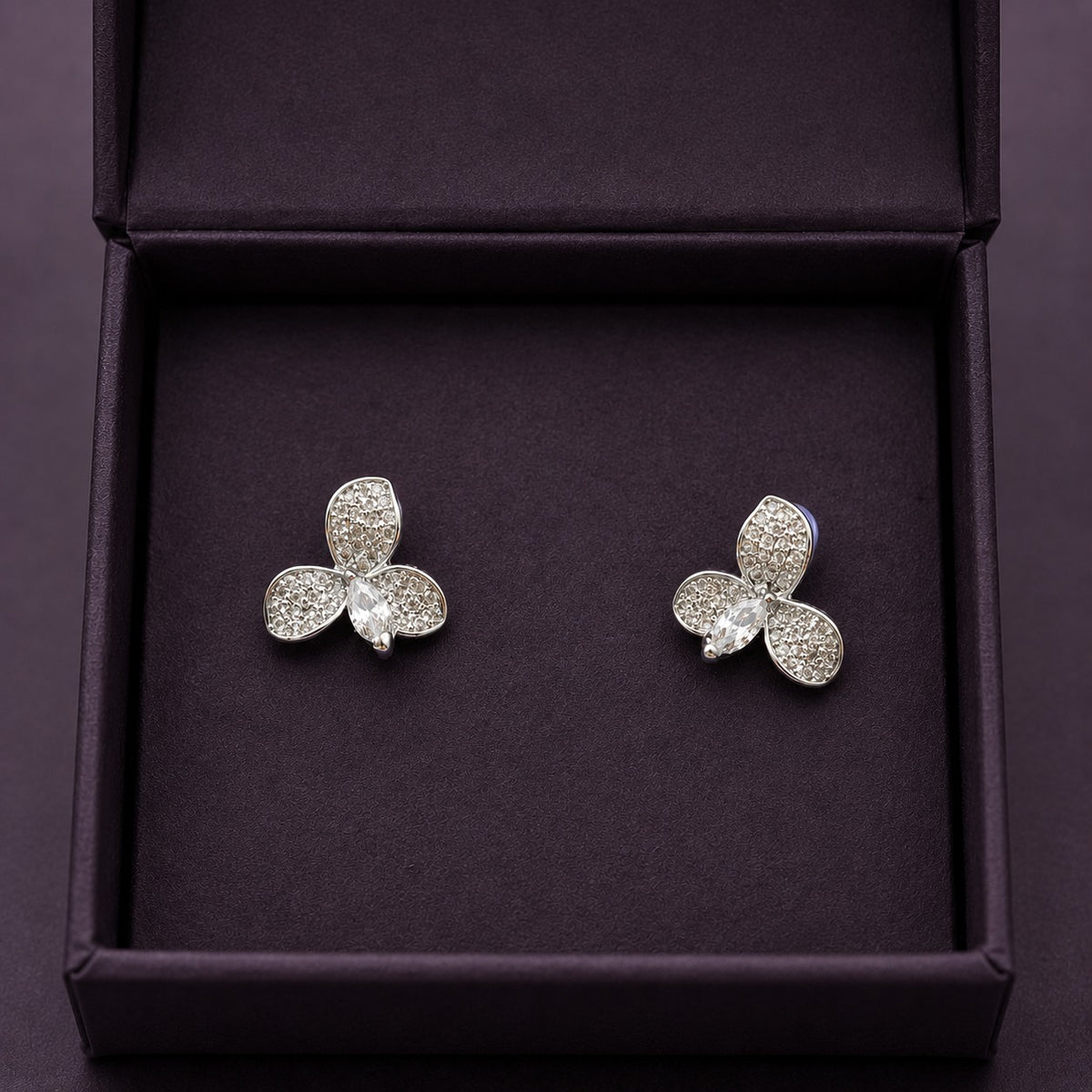 S925 Tria Glint Stud Earrings featuring three zircon-set petal forms with a marquise-cut clear zircon centre, displayed in a deep plum jewellery box.