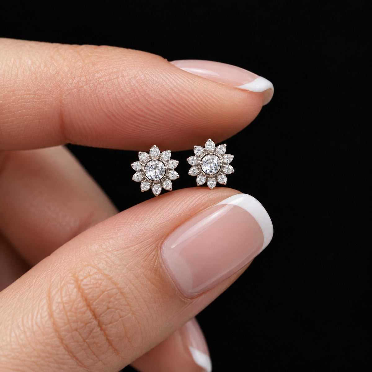 Close-up of petite Solaris Crest Stud earrings held between fingers, showing clear round centre zircons surrounded by marquise-cut stones in a silver-tone setting.